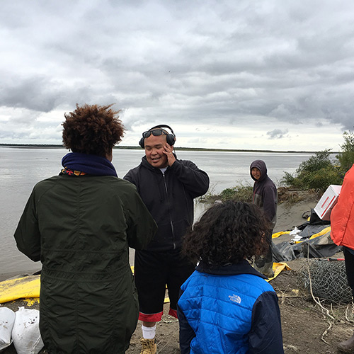 Tracy K. Smith hands a copy of 'American Journal' to a man on the shore of Napakiak, Alaska. August 28, 2018. Credit: Guy Lamolinara.